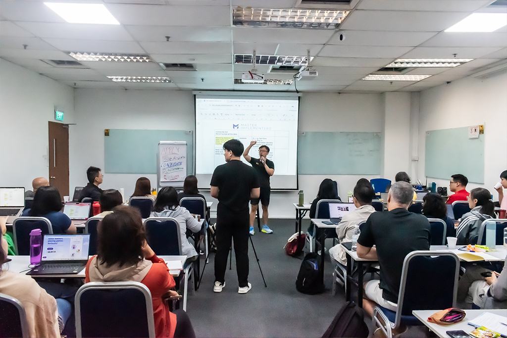 A Master Implementers group with Marc seated at the front of a classroom.